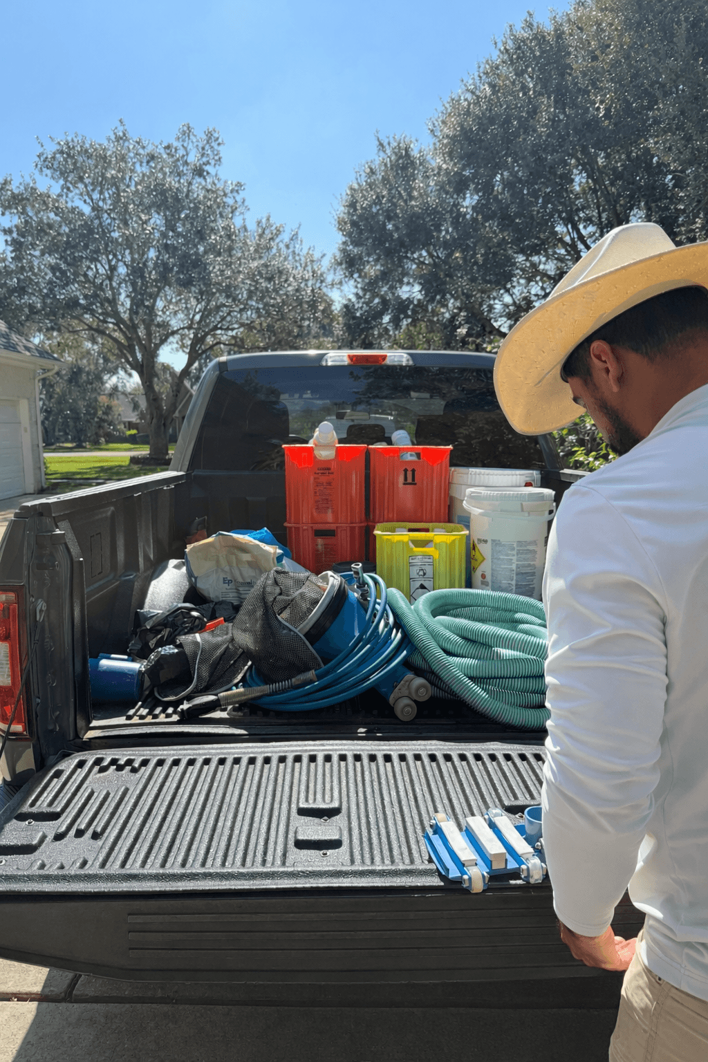 Pool technician with truck bed loaded with pool service equipment — hoses, chemicals, test kits